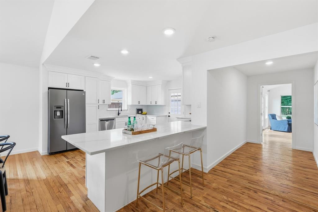 6811 Patrick Drive Dallas, TX 75214 - Photo 16 of 40 Kitchen featuring stainless steel appliances, a breakfast bar area, white cabinets, light wood-style floors, and decorative backsplash