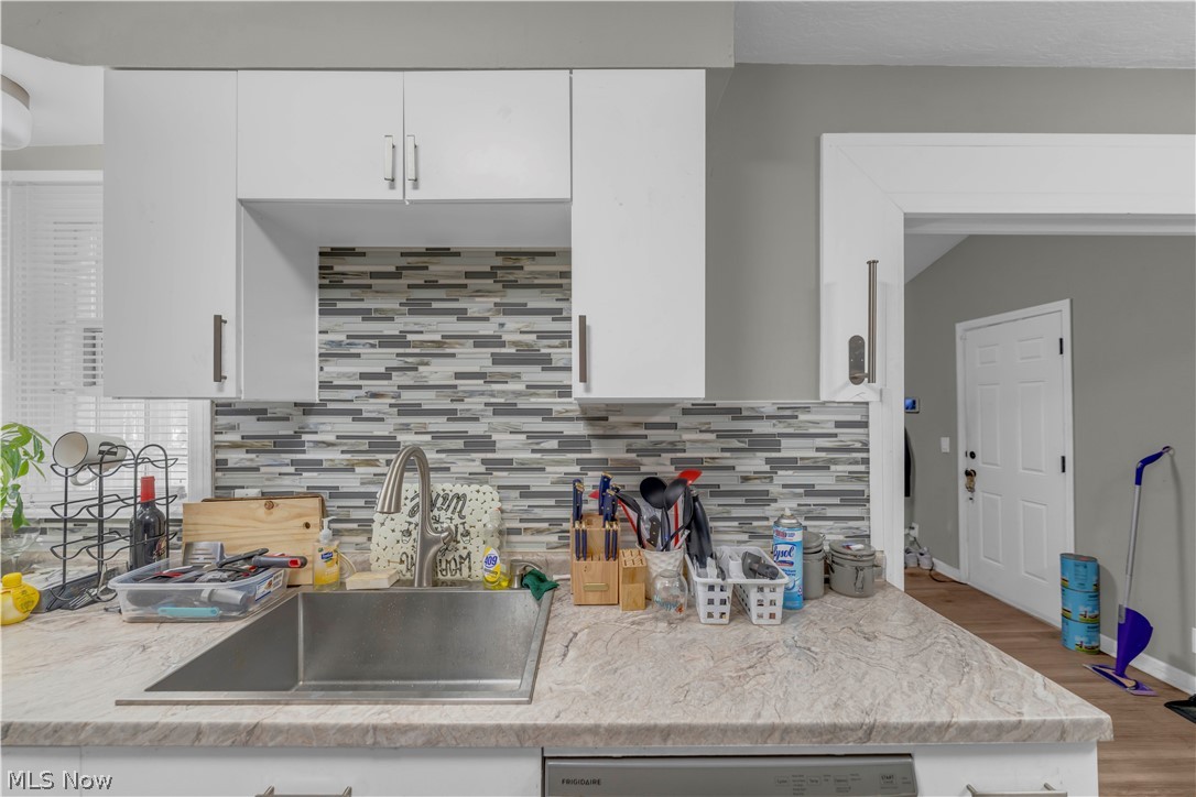 3731 Lowell Road Cleveland Heights, OH 44121 - Photo 14 of 29 White upper cabinetry with contemporary hardware, multi-tone linear tile backsplash, stainless steel sink with gooseneck faucet, light-toned countertop, and wood-finish flooring