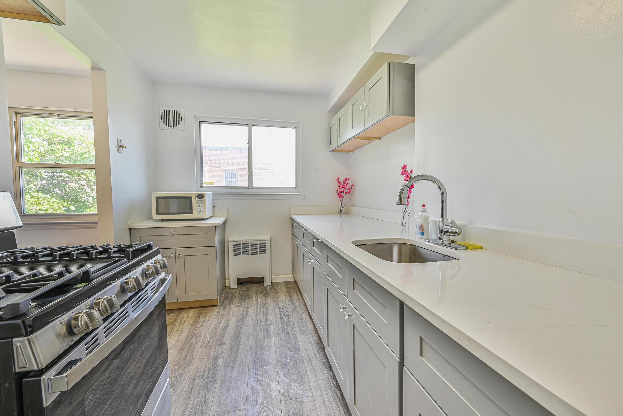 150-01 Horace Harding Expressway Queens, NY 11367 - Photo 6 of 17 Kitchen with gas range, white microwave, healthy amount of natural light, and gray cabinetry