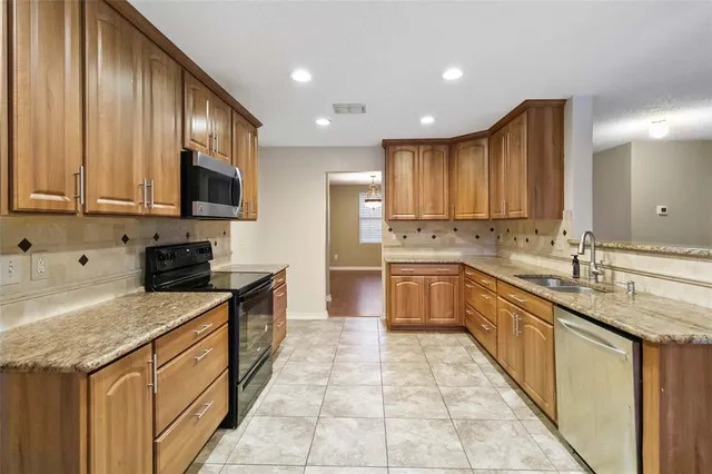 a large kitchen with stainless steel appliances granite countertop a stove top oven a sink dishwasher and a refrigerator with wooden cabinets