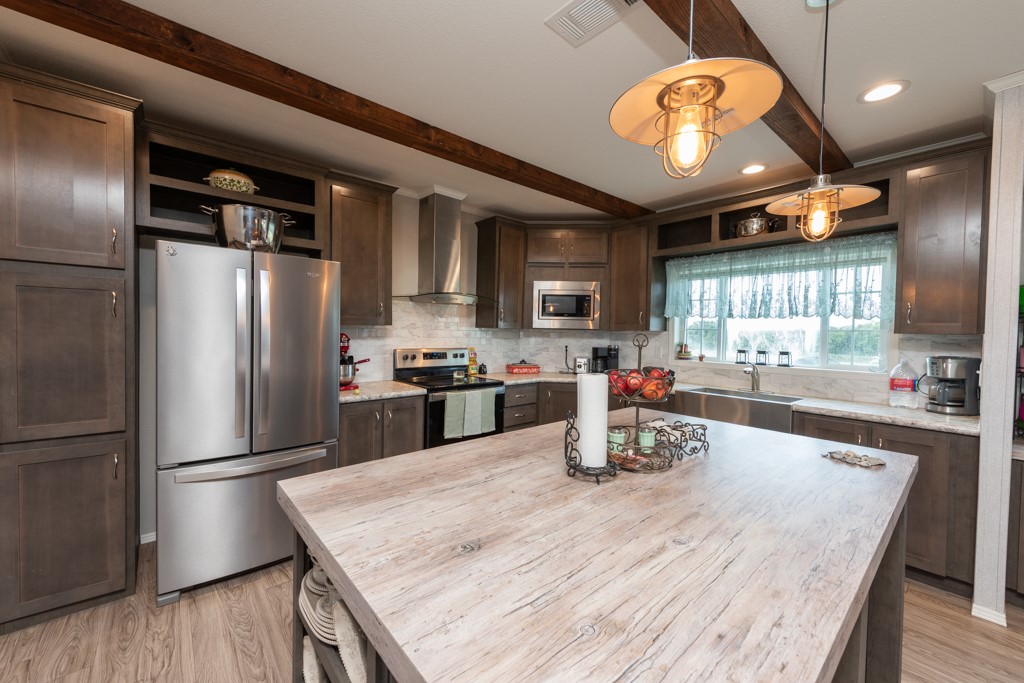 859 Ivy Switch Road Luling, TX 78648 - Photo 12 of 29 Kitchen featuring stainless steel appliances, dark brown cabinetry, beamed ceiling, wall chimney range hood, and hanging light fixtures