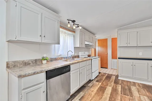 a kitchen with granite countertop a sink stainless steel appliances white cabinets and a window