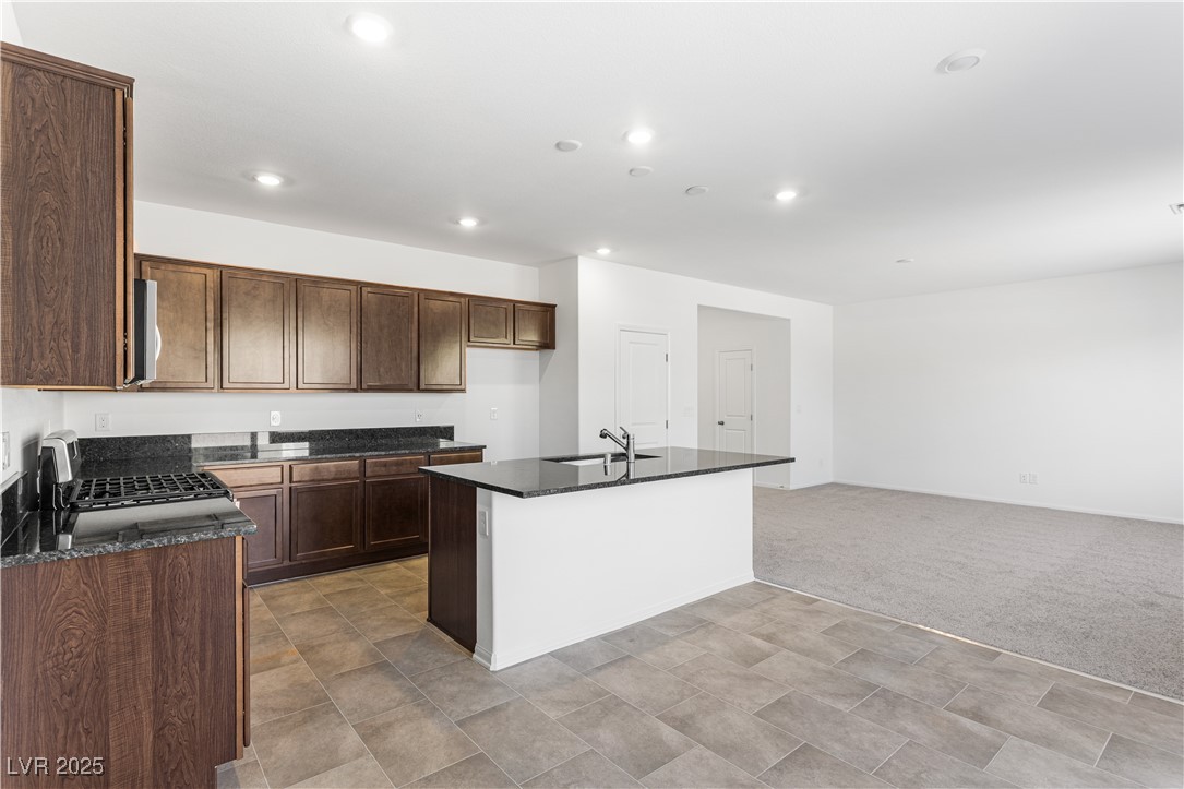 5678 Spring Trellis Street Las Vegas, NV 89113 - Photo 5 of 22 Kitchen with a kitchen island with sink, gas range, dark stone counters, light colored carpet, and recessed lighting