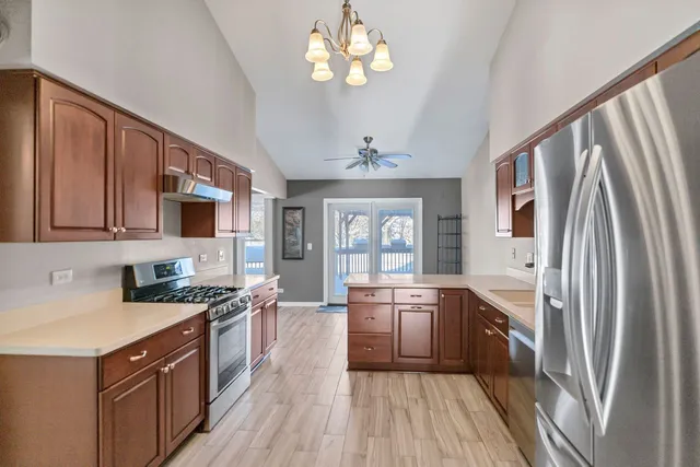 a kitchen with stainless steel appliances granite countertop a refrigerator a sink dishwasher a stove and white countertops with wooden floor