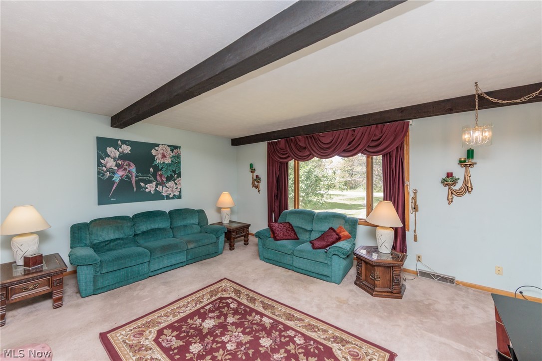 2170 Norton Road Stow, OH 44224 - Photo 23 of 48 Living area featuring exposed ceiling beams, a large window with draped valance, wall-mounted sconces, a central chandelier, and light-colored carpet flooring