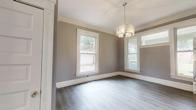 an empty room with wooden floor chandelier and windows