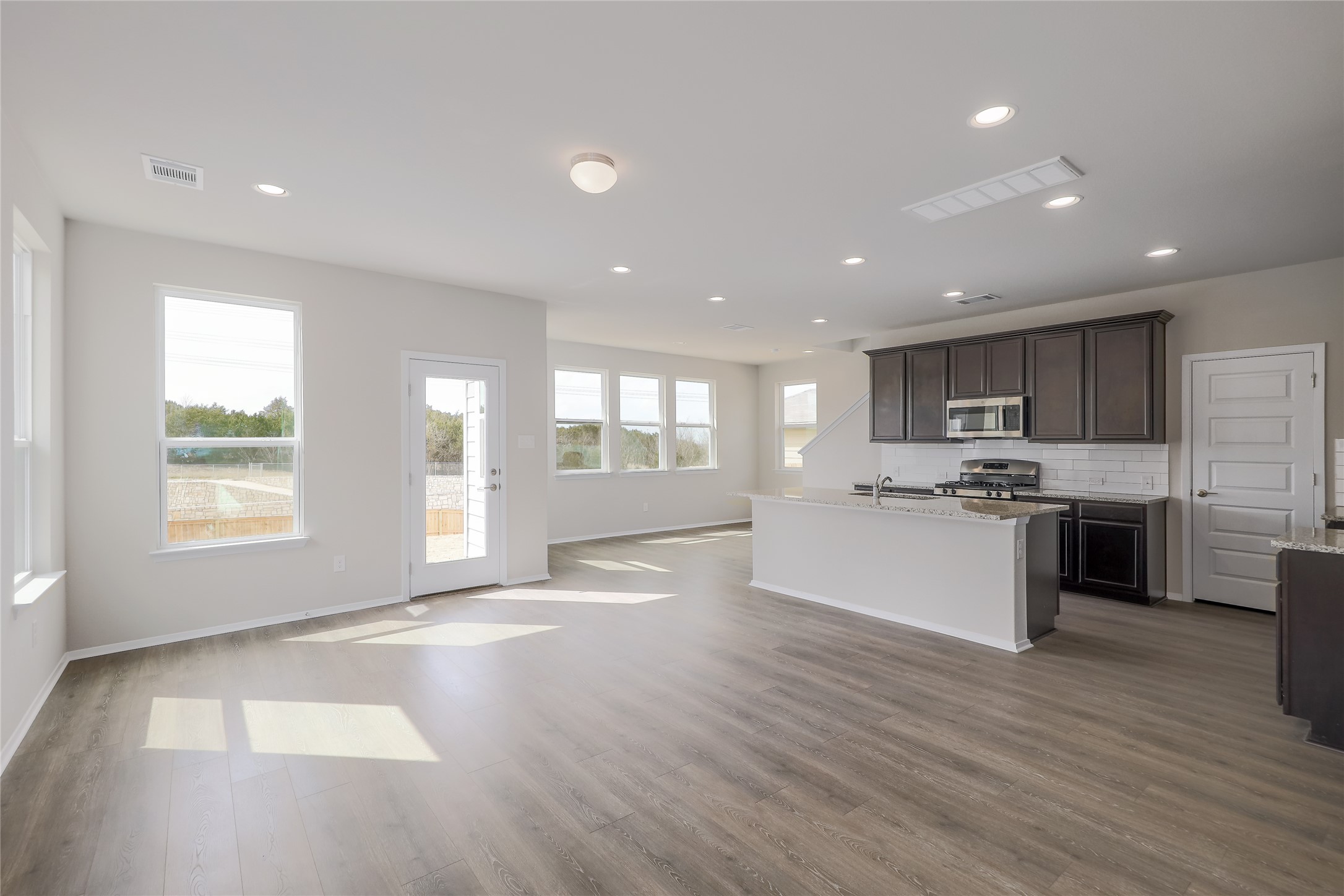 11416 Milano Drive Austin, TX 78747 - Photo 24 of 25 Kitchen featuring a center island with sink, decorative backsplash, open floor plan, light stone counters, and recessed lighting