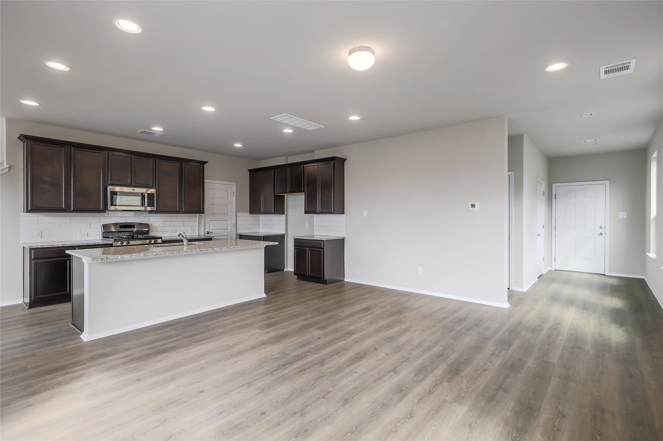 11416 Milano Drive Austin, TX 78747 - Photo 4 of 25 Kitchen with tasteful backsplash, dark brown cabinets, a center island with sink, appliances with stainless steel finishes, and light wood-style flooring