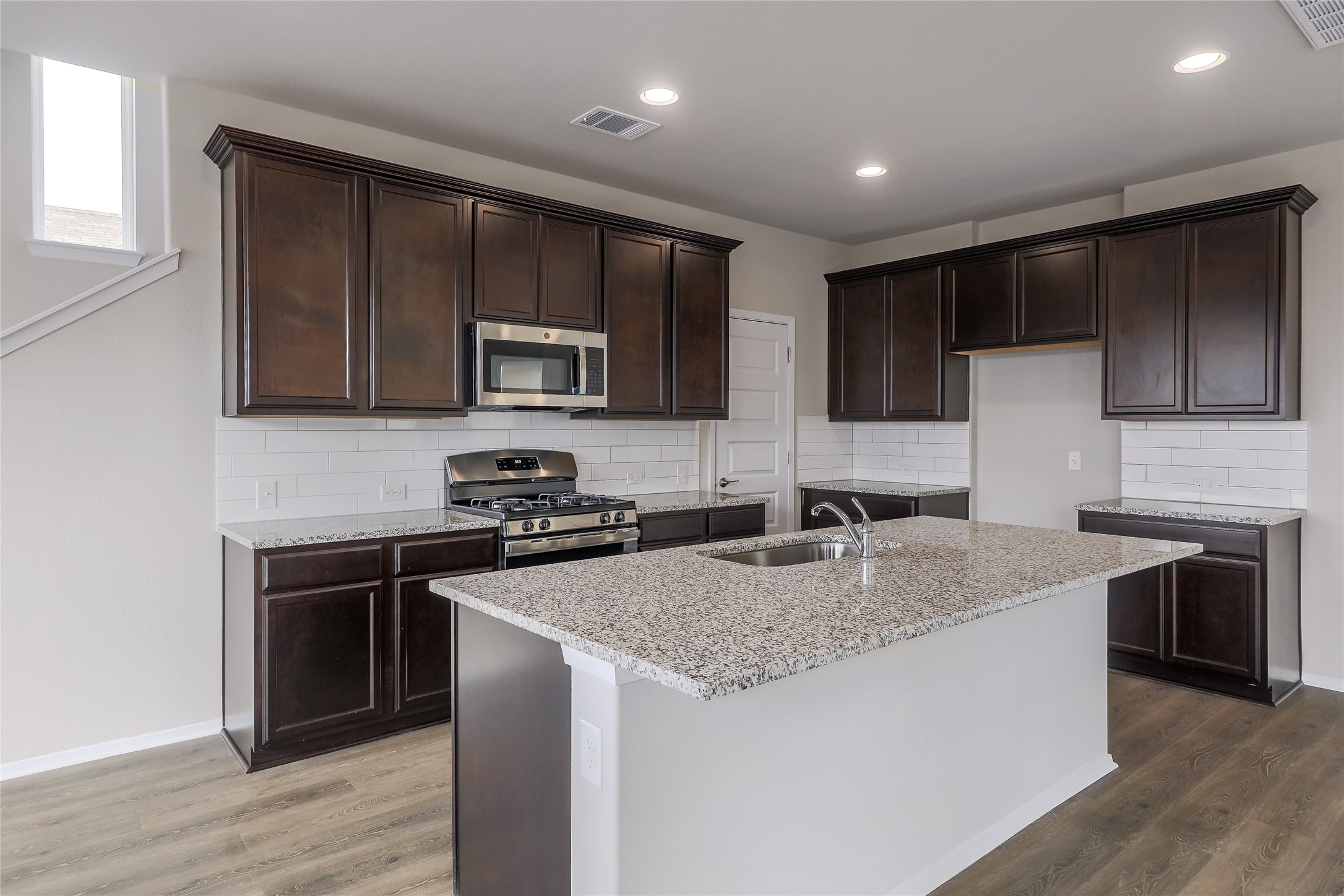 11416 Milano Drive Austin, TX 78747 - Photo 7 of 25 Kitchen featuring backsplash, appliances with stainless steel finishes, light stone counters, light wood finished floors, and recessed lighting