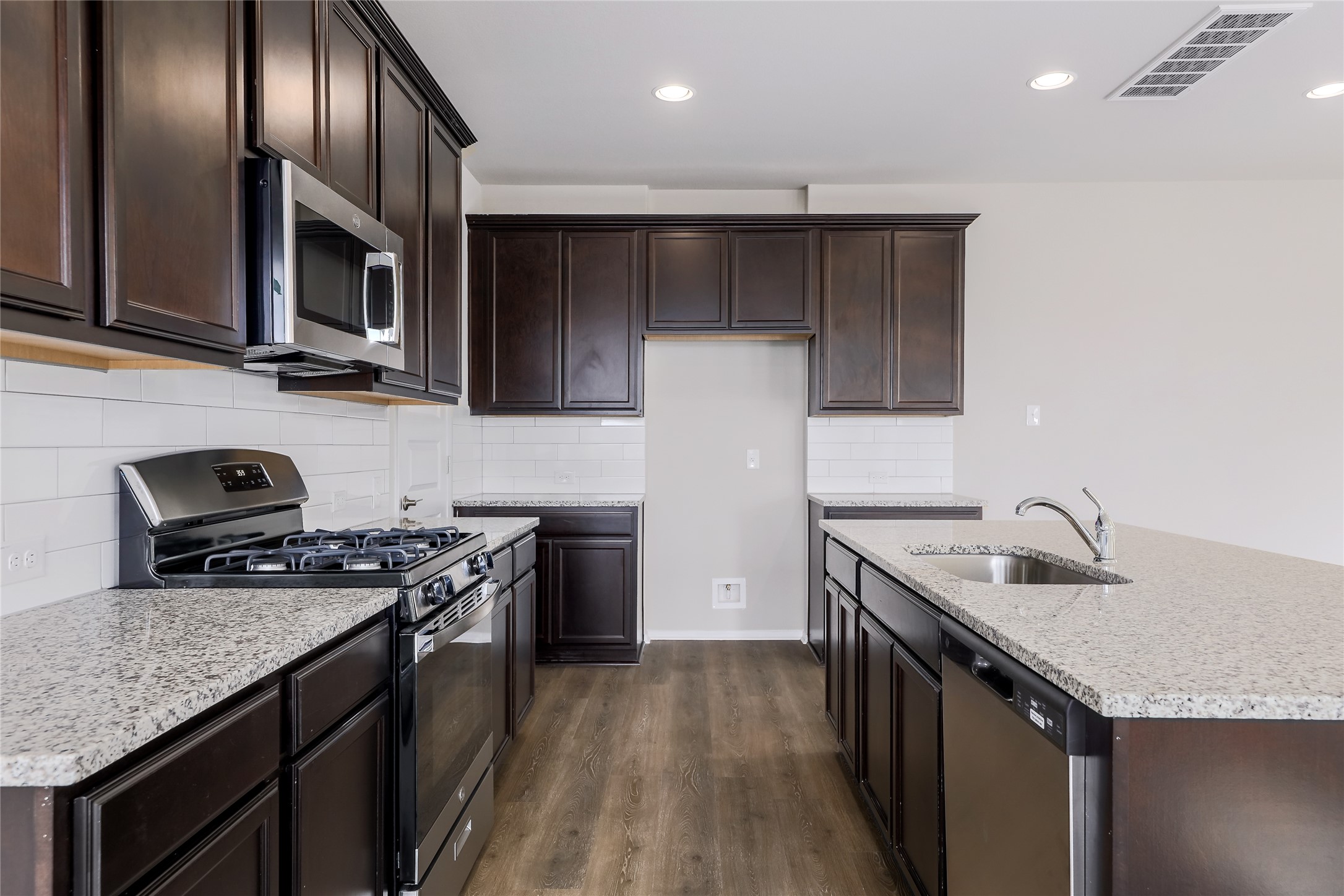 11416 Milano Drive Austin, TX 78747 - Photo 8 of 25 Kitchen with appliances with stainless steel finishes, dark brown cabinetry, dark wood-style flooring, light stone countertops, and recessed lighting