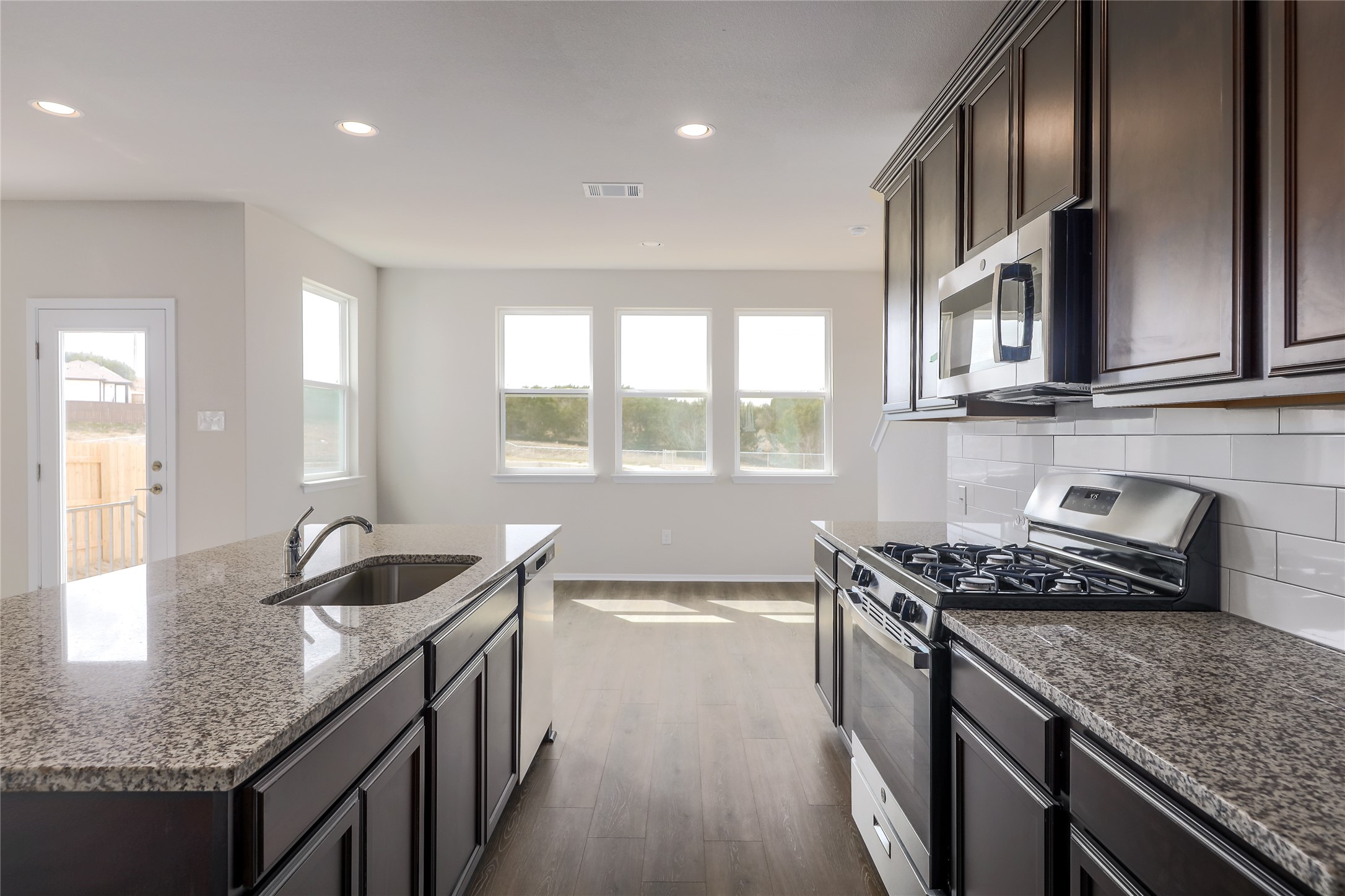 11416 Milano Drive Austin, TX 78747 - Photo 9 of 25 Kitchen featuring stainless steel appliances, dark stone counters, recessed lighting, dark wood finished floors, and an island with sink