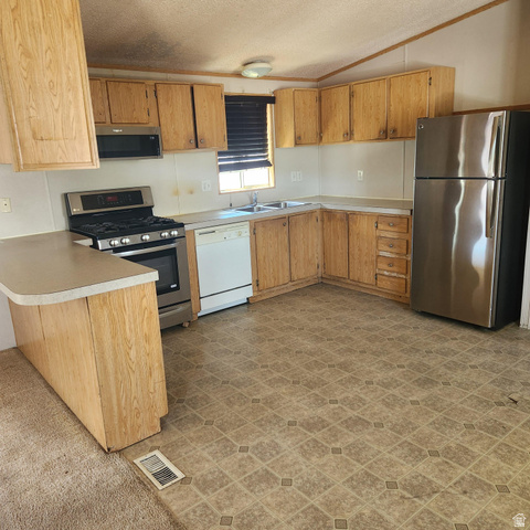 3760 Gold Ridge Drive, Unit 82 Magna, UT 84044 - Photo 12 of 29 Kitchen featuring wood-finish cabinetry, a double basin sink, a gas range with a microwave above, a dishwasher, and a stainless steel refrigerator