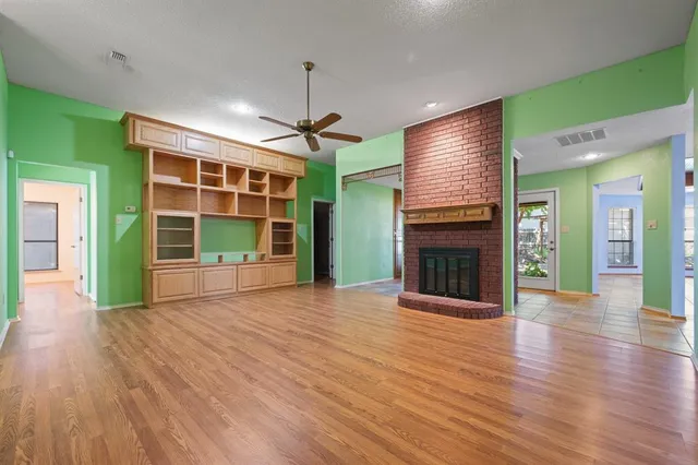 a view of an empty room with wooden floor fireplace and a window