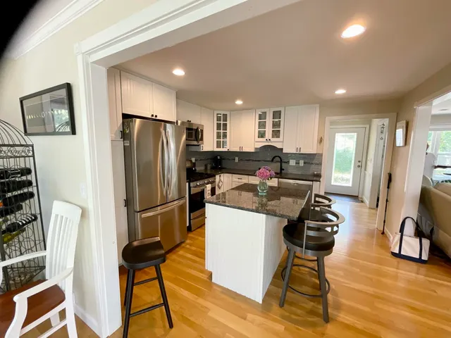 a kitchen with stainless steel appliances kitchen island granite countertop a refrigerator a stove a sink dishwasher and a dining table with wooden floor