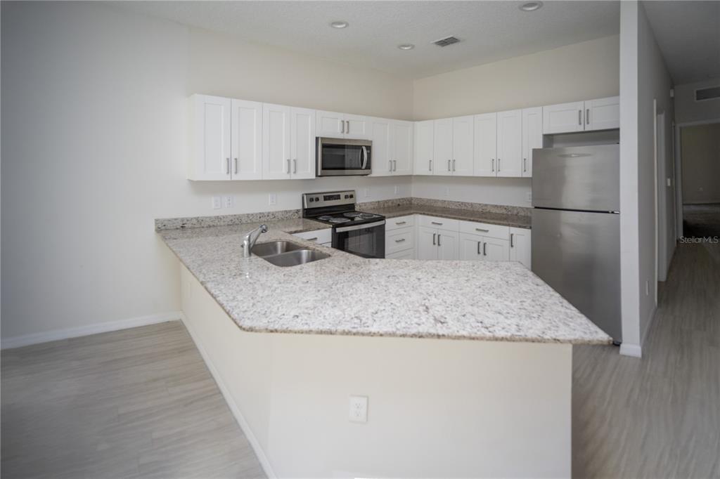2148 Penny Lane Kissimmee, FL 34741 - Photo 5 of 15 a kitchen with stainless steel appliances granite countertop a sink a microwave a refrigerator and white cabinets