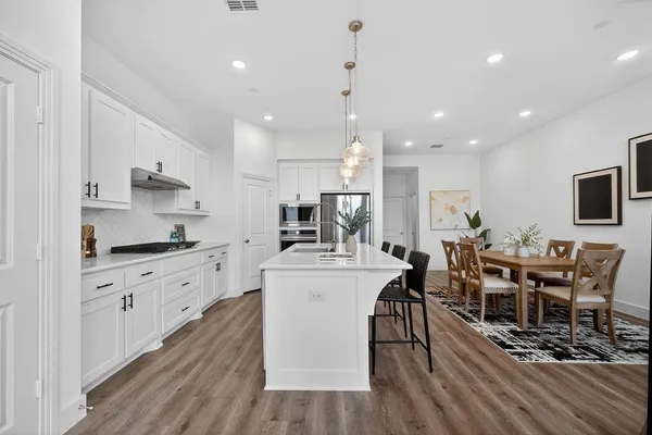 a kitchen with stainless steel appliances a dining table chairs stove refrigerator and cabinets