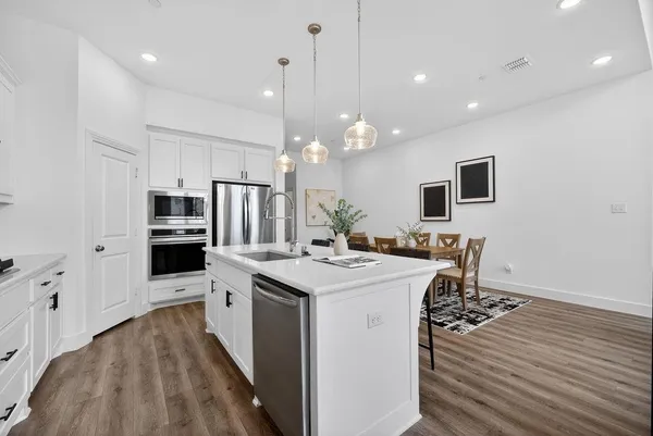 a kitchen with stainless steel appliances a stove top oven a refrigerator a sink and white cabinets with wooden floor