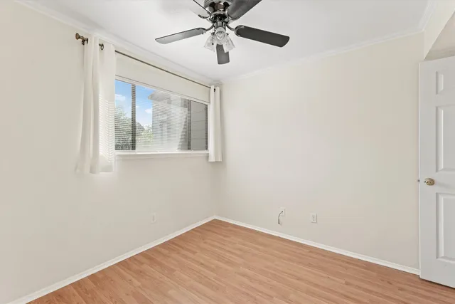 a view of an empty room with wooden floor and a ceiling fan