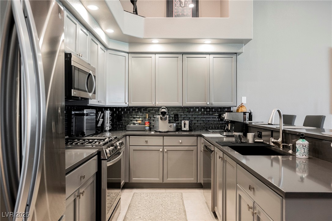 7625 Rolling View Drive, Unit 202 Las Vegas, NV 89149 - Photo 7 of 28 Kitchen featuring stainless steel appliances, gray cabinets, decorative backsplash, a peninsula, and dark stone countertops