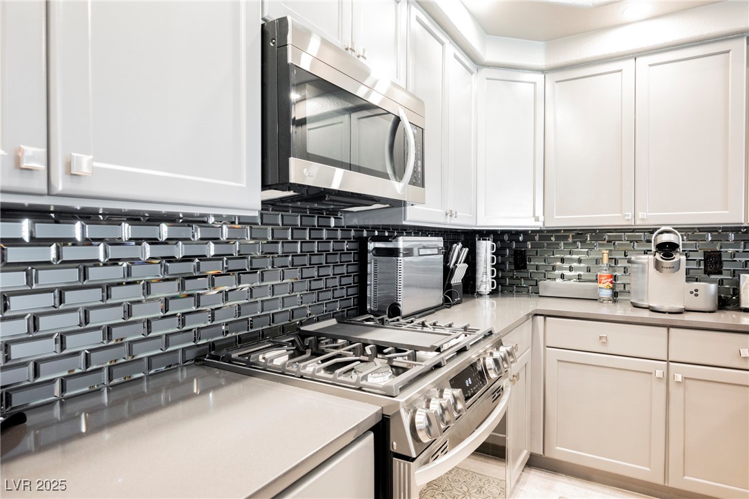 7625 Rolling View Drive, Unit 202 Las Vegas, NV 89149 - Photo 8 of 28 Kitchen featuring appliances with stainless steel finishes, tasteful backsplash, white cabinetry, and light stone countertops