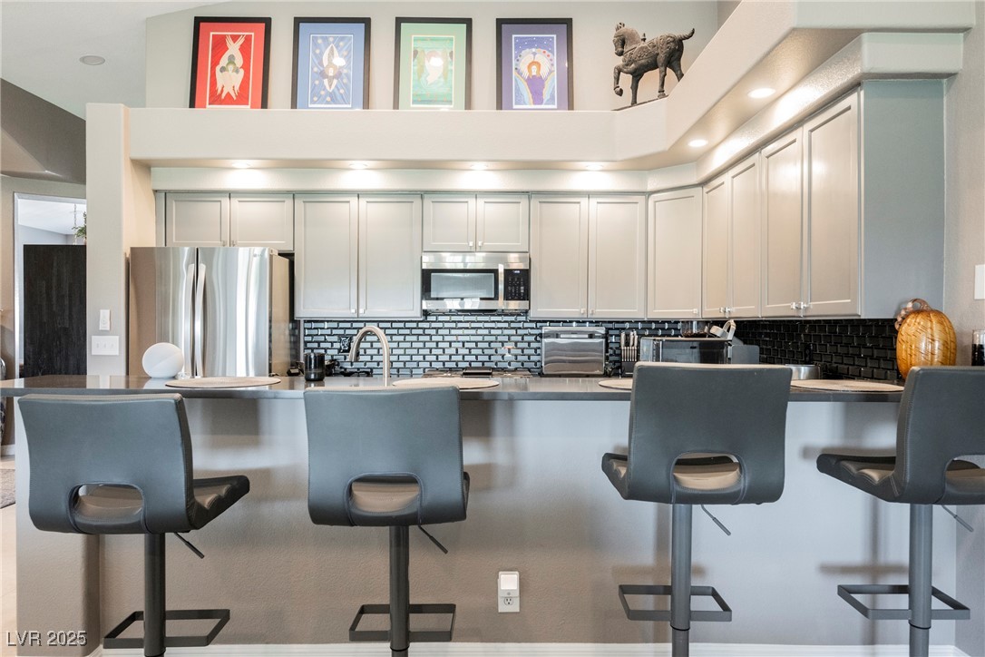 7625 Rolling View Drive, Unit 202 Las Vegas, NV 89149 - Photo 9 of 28 Kitchen featuring a breakfast bar, backsplash, appliances with stainless steel finishes, white cabinetry, and a peninsula