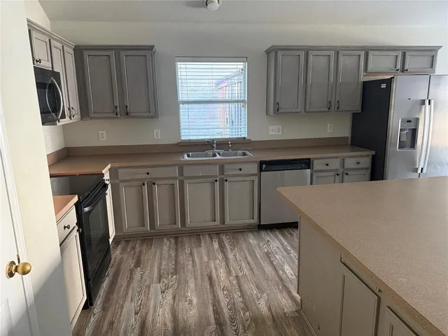 a kitchen with stainless steel appliances a refrigerator a sink a stove a microwave and wooden floors