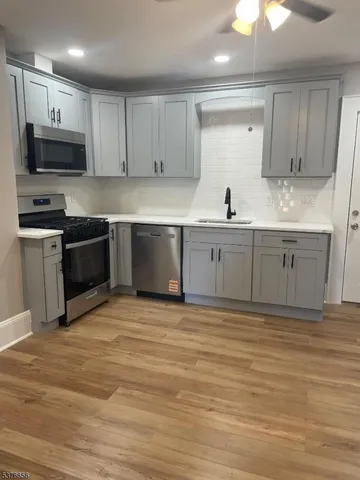 a large kitchen with granite countertop a stove top oven a sink and dishwasher white cabinets with wooden floor