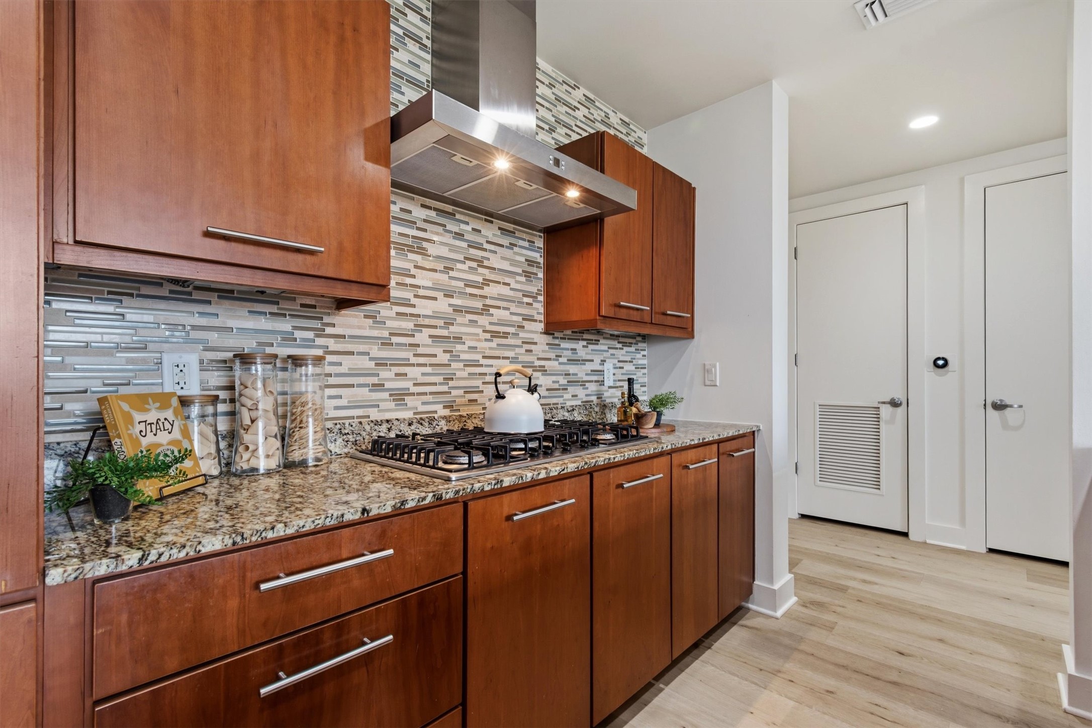 210 Lee Barton Drive, Unit 517 Austin, TX 78704 - Photo 11 of 30 Rich wood cabinetry and stone backsplash highlight this well-appointed kitchen with premium appliances and luxury vinyl plank flooring.