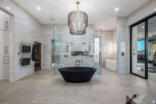 2867 East Granite Way St. George, UT 84790 - Photo 27 of 69 Spacious bathroom featuring a central black freestanding soaking tub, a large walk-in glass shower enclosure with multiple shower heads, a built-in sauna, light-colored large format tile flooring, and a tiered chandelier