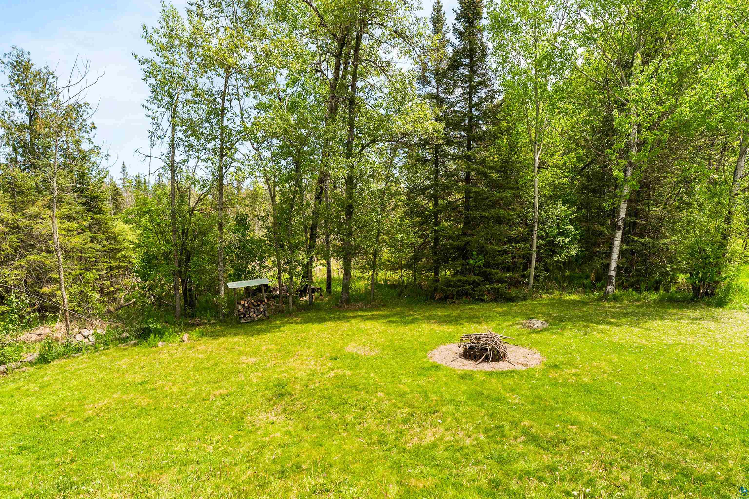 4808 Midway Road Duluth, MN 55811 - Photo 47 of 57 Expansive green lawn framed by mature trees, featuring a defined fire pit area and a wood storage shed