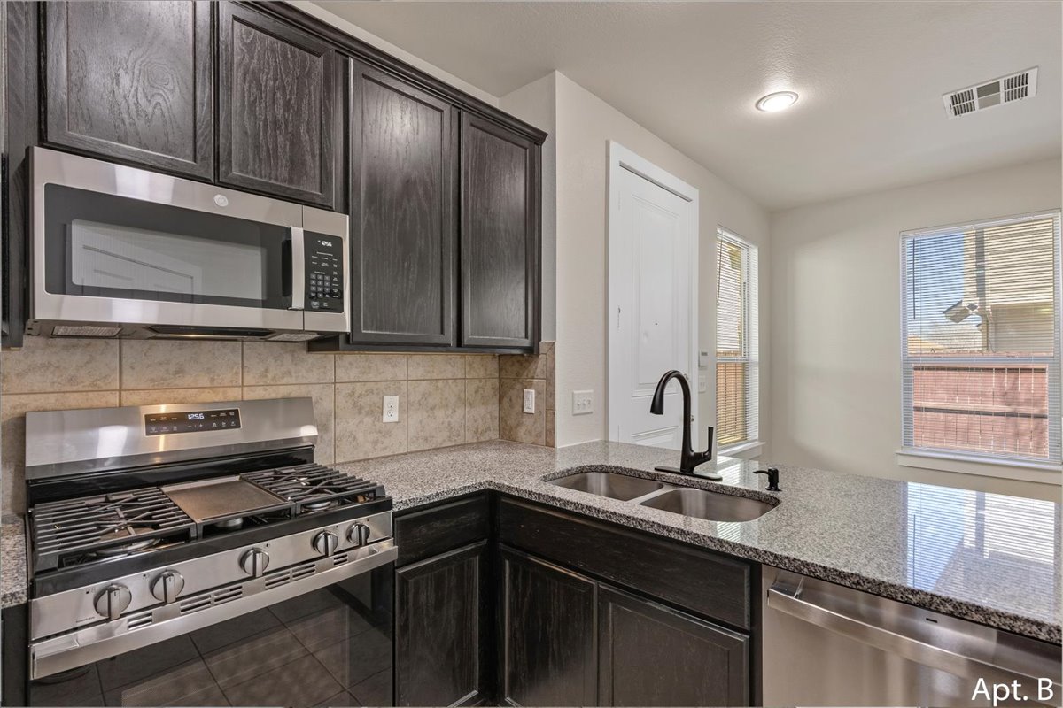 2225 Katy Lane, Unit B Georgetown, TX 78626 - Photo 10 of 22 Kitchen with stainless steel appliances, light stone counters, backsplash, tile patterned floors, and dark wood finish cabinetry