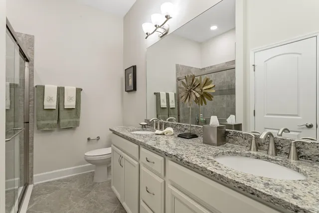 a bathroom with double vanity sink a toilet a mirror and shower
