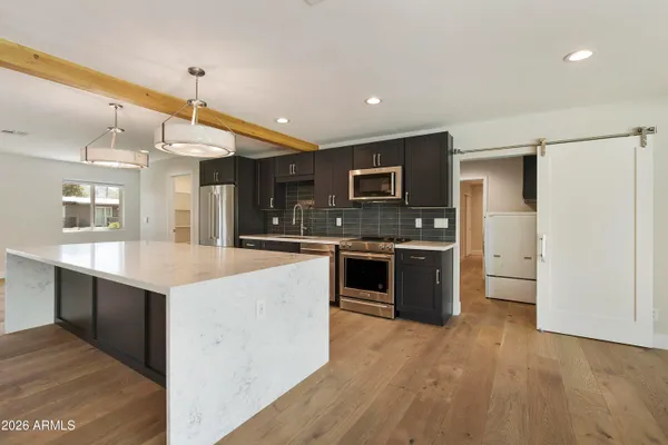 a kitchen with stainless steel appliances a stove top oven a sink dishwasher and a refrigerator with wooden floor