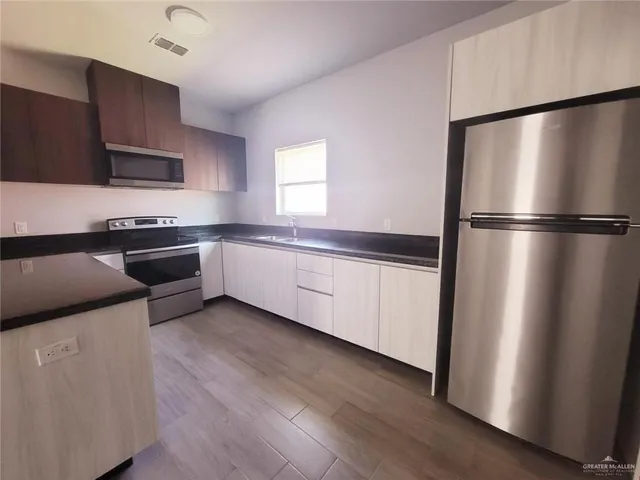 a kitchen with stainless steel appliances a refrigerator a sink a stove a microwave and wooden floors