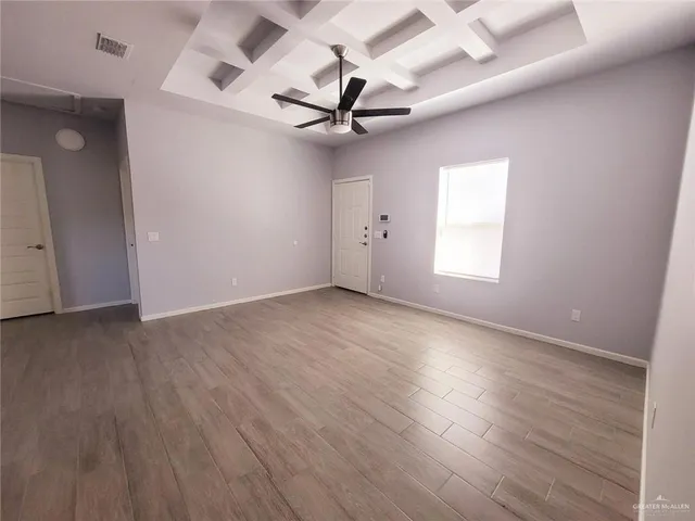 an empty room with wooden floor ceiling fan and windows