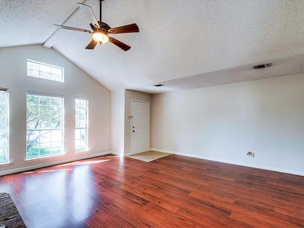 an empty room with wooden floor fan and windows