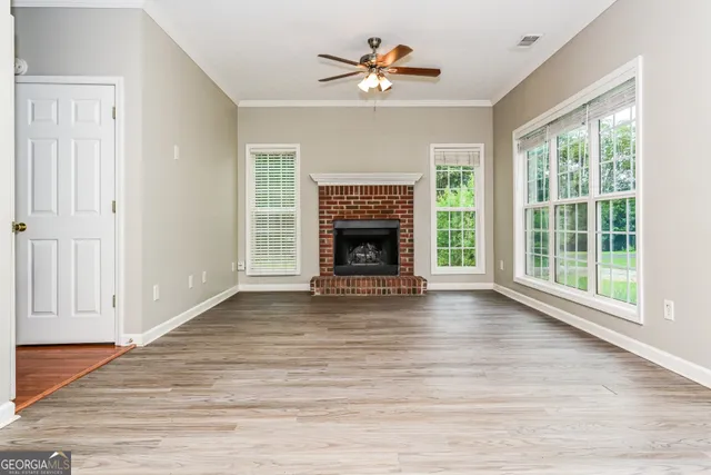 a view of an empty room with wooden floor fireplace and a window