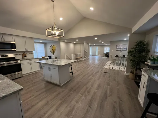 a large kitchen with granite countertop a large center island a sink dishwasher a stove and a refrigerator with wooden floor