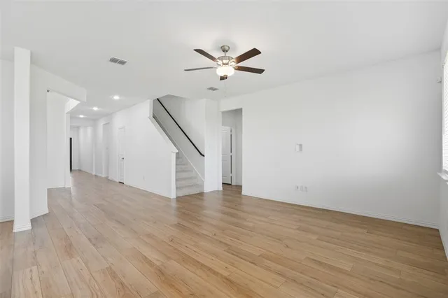 a view of an empty room with wooden floor and a ceiling fan