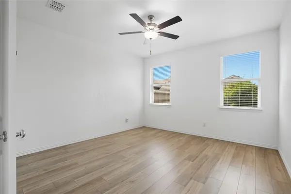 an empty room with wooden floor ceiling fan and windows