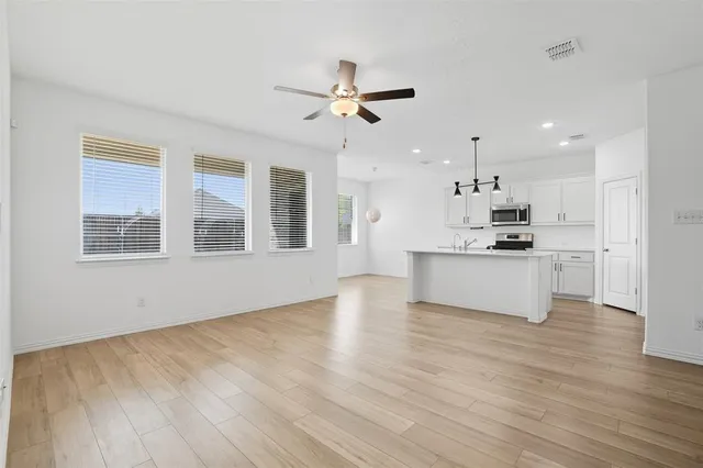 a view of an empty room with wooden floor and a kitchen