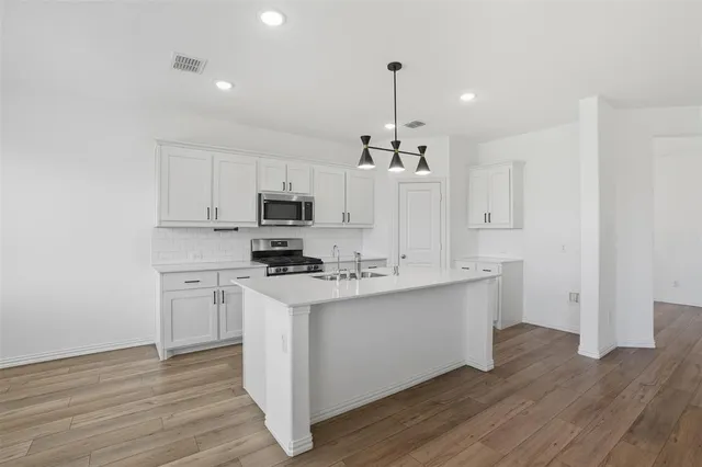 a kitchen with stainless steel appliances a stove top oven a sink a refrigerator and white cabinets with wooden floor