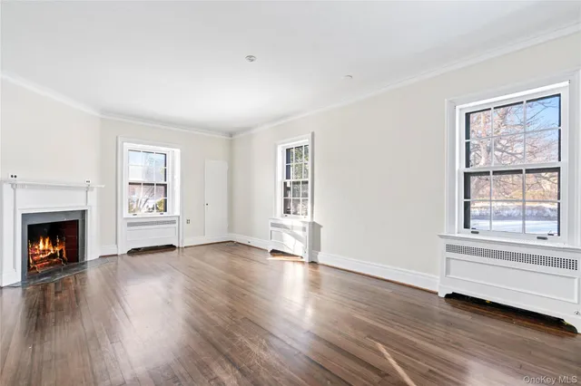 a view of an empty room with wooden floor fireplace and a window