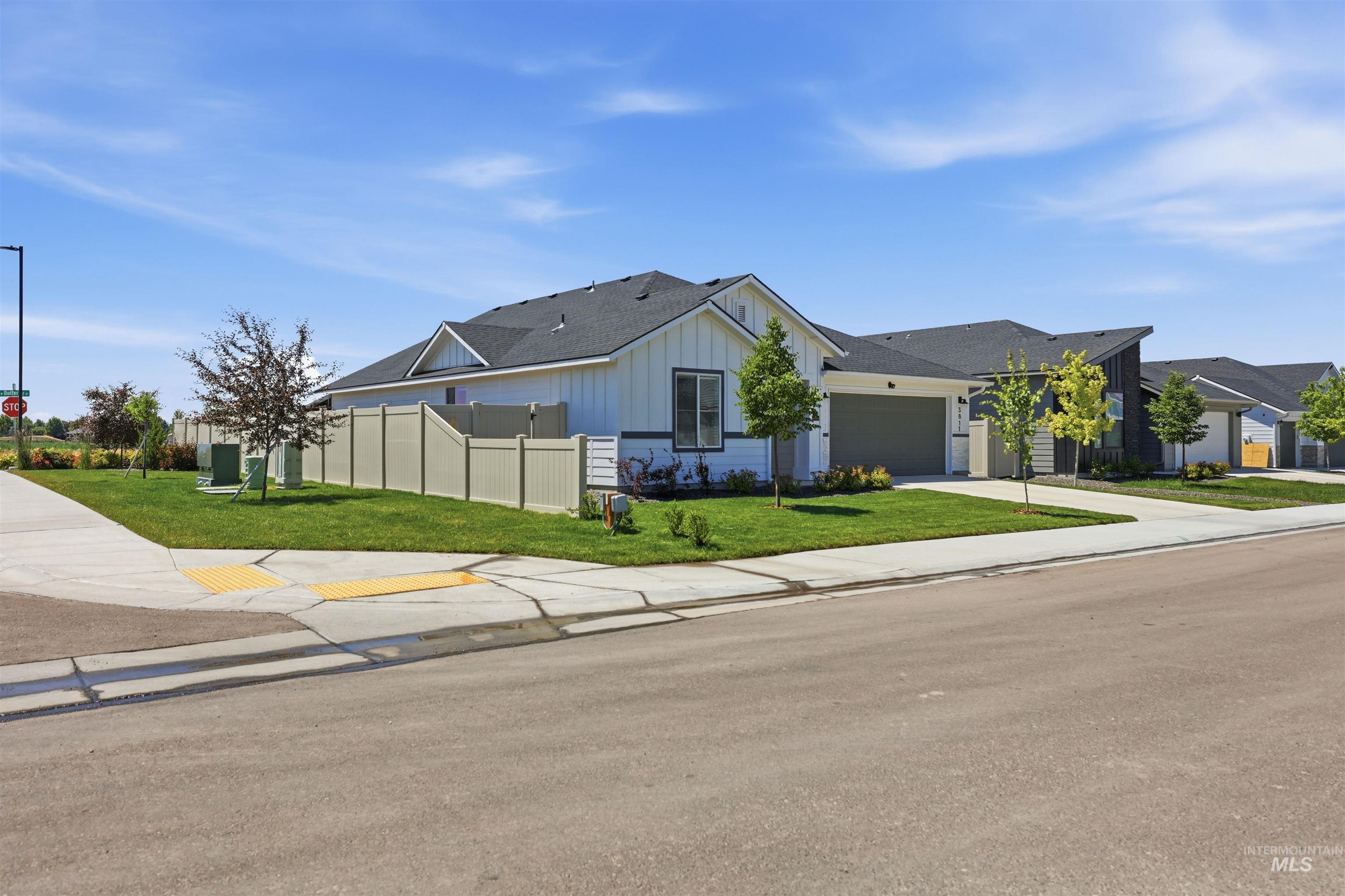 3811 West Maypearl Street Meridian, ID 83642 - Photo 2 of 39 Contemporary-style residence featuring a white vertical siding exterior with dark trim accents, an attached two-car garage, mature landscaping, a private fenced yard, and concrete sidewalks