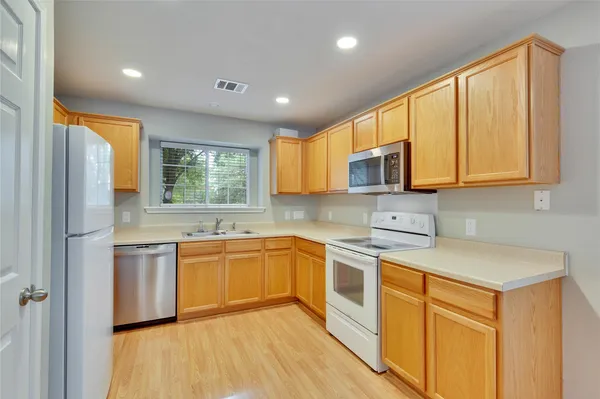 a kitchen with stainless steel appliances granite countertop wooden cabinets a sink dishwasher a refrigerator and a microwave oven with wooden floor