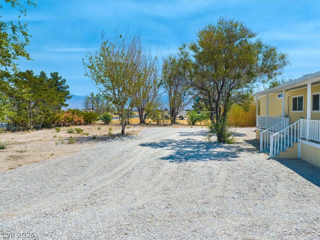 4081 Retread Road Pahrump, NV 89048 - Photo 70 of 98 A welcoming front porch leads to a spacious gravel driveway, framed by mature trees and mountain views.