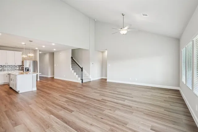 a view of an empty room with wooden floor and a kitchen view