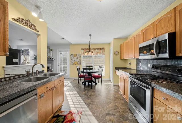 a kitchen with stainless steel appliances granite countertop a stove top oven a sink dishwasher a dining table and chairs with wooden floor