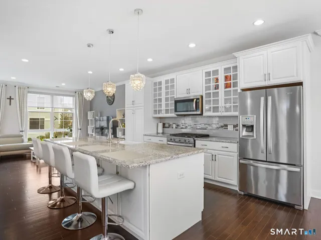 a kitchen with stainless steel appliances granite countertop a refrigerator a stove a sink a dining table and chairs with wooden floor