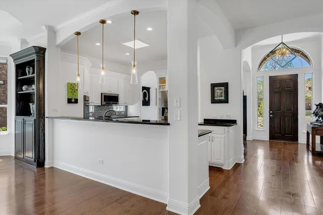 a kitchen with stainless steel appliances granite countertop a refrigerator a sink and white cabinets with wooden floor